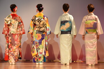 Four Japanese women with black hair wearing kimonos and obi belts with traditional floral and...