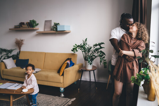Hand length of African American man and Caucasian woman cuddling during weekend leisure in home interior enjoying multicultural family bonding with kid, biracial parents and daughter in living room