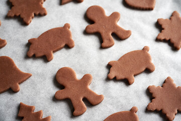 Man and pig shapes cut out from raw pastry dough on a sheet of baking paper - preparation of gingerbread Christmas cookies