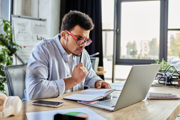 Concentrated man takes notes while working intently on a laptop in a modern office environment.