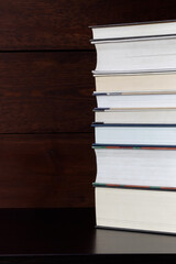 Stack of books on shelf against  wooden wall background. Vertical photo.