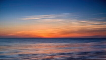 Fototapeta premium Seascape Serenity: A tranquil sunset paints the sky with hues of orange and blue, reflecting on the calm, rippling waters of the ocean. The soft.