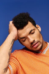 A stylish man relaxes with his hand on his head, set against a vibrant backdrop.