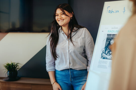 Confident female student presenting a fashion project on a whiteboard in a state-of-the-art learning setting