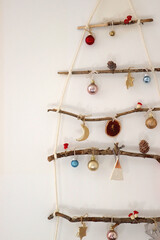 Creative DIY Christmas tree made with branches and decorated with various Christmas ornaments, hanging on the wall.
