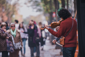 a man playing a violin in the street with a crowd in the background.