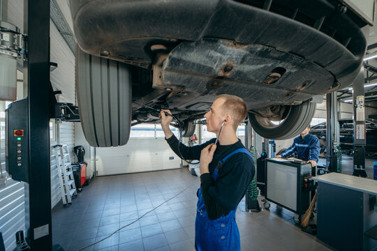 Young car mechanic at repair service station inspecting car wheel and suspension detail of lifted automobile.