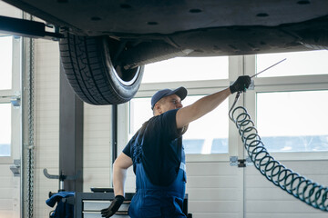 Young car mechanic at repair service station inspecting car wheel and suspension detail of lifted...