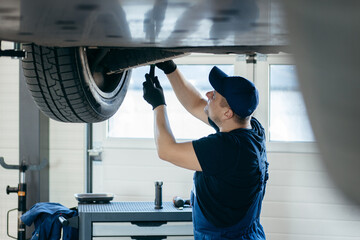 Young car mechanic at repair service station inspecting car wheel and suspension detail of lifted...