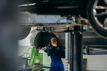 Young car mechanic at repair service station inspecting car wheel and suspension detail of lifted automobile