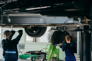 Young car mechanics at repair service station inspecting car wheel and suspension detail of lifted...