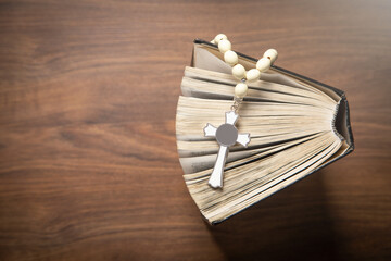 Holy Bible and rosary beads on the wooden background.
