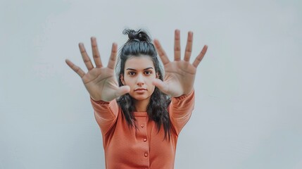 A young woman in an orange sweater stands against a white background with her hands extended forward, emphasizing a stop gesture or creating a sense of motion and expression.