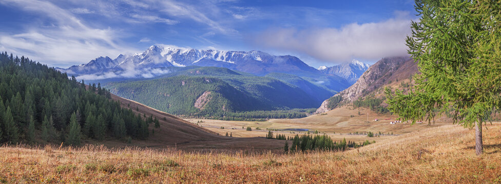 Mountain valley in the morning light, snow-capped mountain peaks in clouds, summer travel, panoramic view	