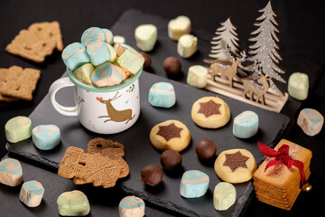 Festive Christmas table arrangement featuring a hot chocolate cup with marshmallows, Christmas lights, Santas,  garlands, and holiday sweets.
