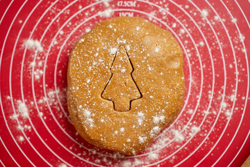 Christmas tree shape cut out in gingerbread dough. Ball of dough dusted with flour on red baking mat, top view