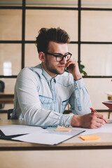 Young male partners working togetherness in office and discussing ideas for startup project, caucasian man holding textbook and explaining information to colleague sitting near and drawing sketches