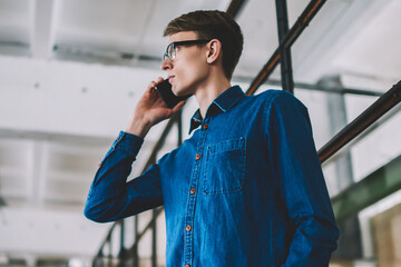 Caucasian male student pondering on news get on telephone conversation using good internet connection, young hipster guy making important call to customer support for checking banking balance