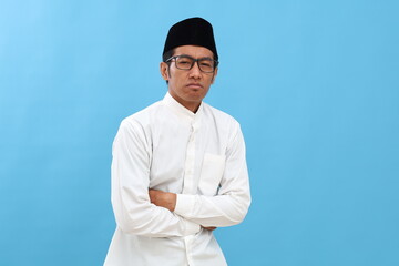 Sad asian muslim man standing while holding his stomach. Isolated on blue with copyspace