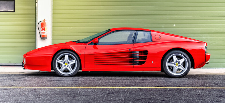 Red Ferrari 512 sports car on the race track. Fast luxury classic car Ferrari Testarossa parked outside in front of the garage.