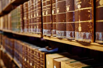 Row of aged leather-bound books on wooden shelf in library