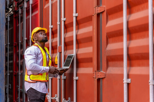 african man in safety gear and hardhat using tablet computer at container cargo,foreman checking electronic seal on container box,worker working in shipping yard