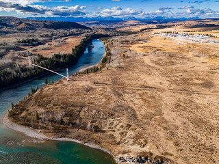Natural gas pipeline crossing over river leaving a distant gas plant industrial site transporting natural resources overlooking the Canadian Rocky Mountains near Cochrane Alberta Canada..