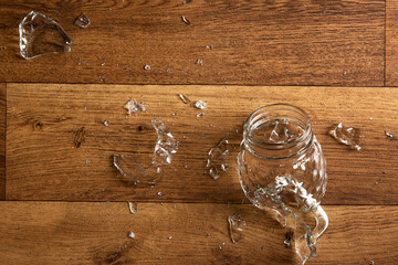 Shattered mason glass jar on a wooden floor. Scattered broken pieces of smashed mug. Symbol of...