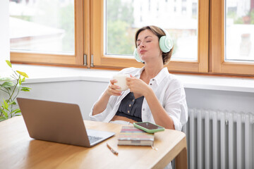 Tired and bored attractive woman sitting at the table and working on laptop in the kitchen at home	