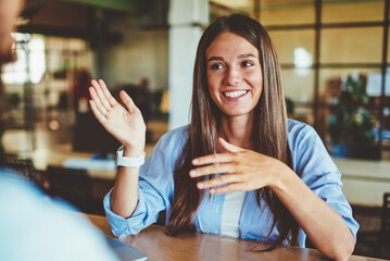 Happy successful hipster girl explaining information to male friend sitting in front, positive man...