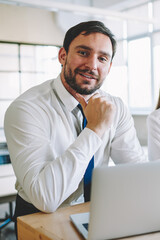 Portrait of successful positive male professional architect sitting at desktop with laptop computer...