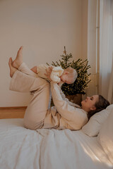 Mother with child on bed against Christmas tree, light vertical photo