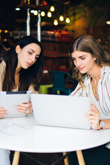 Caucasian freelancers have collaboration meeting for brainstorming in coffee shop with high speed internet connection, skilled female colleagues discussing webinar information watching video on laptop