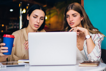 Skilled women watching tutorial webinar during e learning in coffee shop concentrated on received education information, Caucasian freelancers reading web publication discussing business ideas
