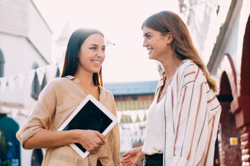 Cheerful female friends 20s enjoying live communication during random meeting in city town, happy casual dressed women fellows discussing relations feelings during live conversation at street