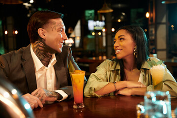 A diverse, tattooed couple enjoys cocktails and joyful moments on a fun night out.
