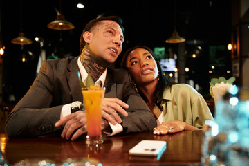 A young multicultural couple shares a cozy moment on a night out at a lively bar.