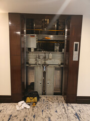 Maintenance crew is working on an elevator system in a hotel corridor with tools and equipment nearby