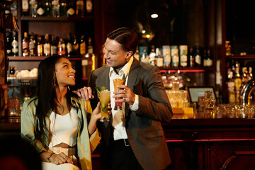 A multicultural couple shares a joyful moment while sipping cocktails at a cozy bar atmosphere.