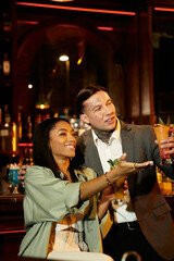 Tattooed couple shares laughter and drinks, enjoying a lively night at the bar indoors.