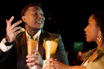 Young multicultural couple shares laughter and drinks on a lively evening date.