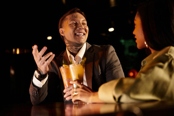 Tattooed man and woman share laughter and drinks while enjoying their evening out together.