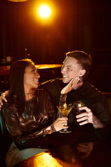 A young couple shares a joyful moment over drinks in a lively bar.