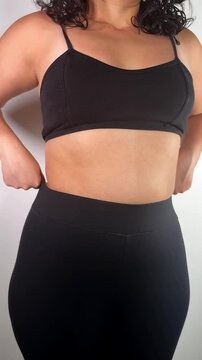 Close-up of a woman pulling up her black leggings, subtly adjusting to cover stomach rolls, promoting a natural and relatable body image.