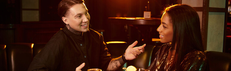 Tattooed man and woman share laughter and drinks on a cozy evening date in a lively bar.