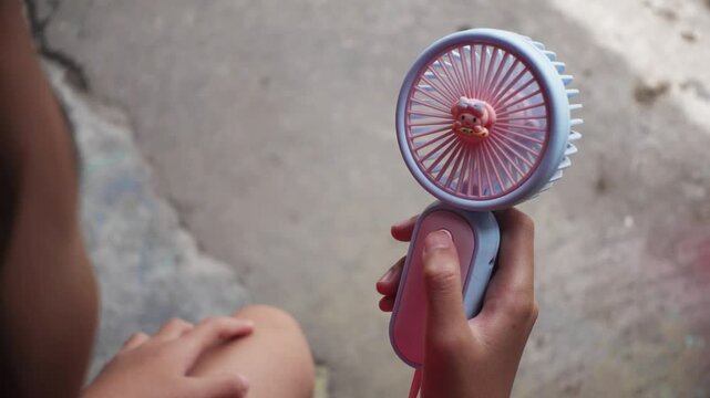 A hand is holding a portable fan and turn on. Presses the power button on a portable portable fan
