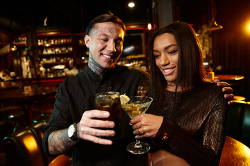 Young couple shares cheerful moments while savoring cocktails in a lively bar atmosphere.