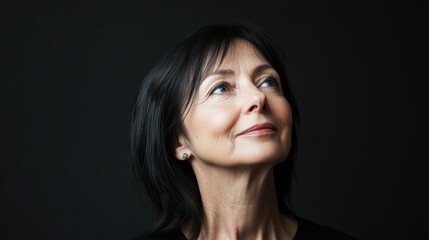 Fototapeta premium Serene portrait of a 60 years old woman against black background