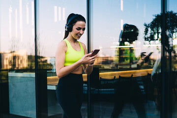 Cheerful millennial female doing sport walking outdoors using cellphone device for messaging and...