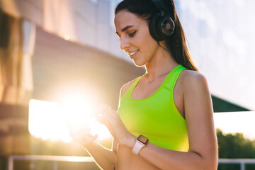 Smiling Caucasian woman enjoying time for morning training on sunny day downloading music to...